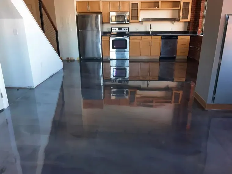 Dark metallic epoxy floor running through a kitchen with exposed brick